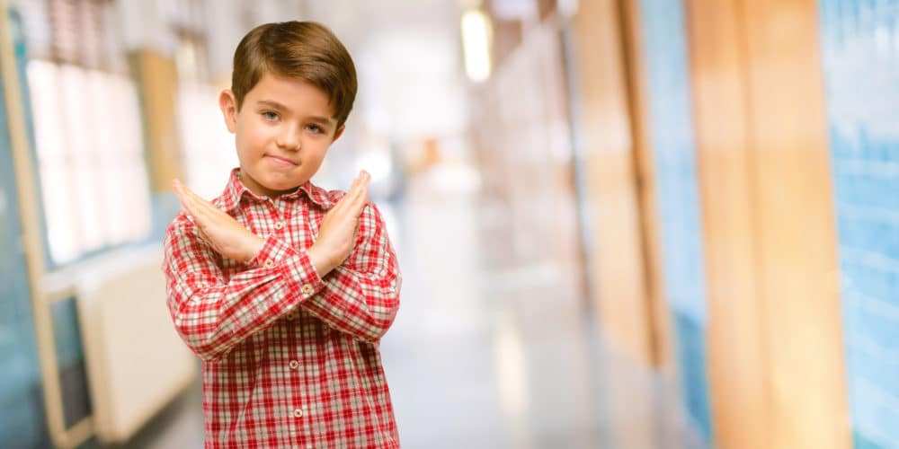 Handsome toddler child with green eyes annoyed with bad attitude making stop sign crossing hands, saying no, expressing security, defense or restriction Schools safety with CrisisAlert