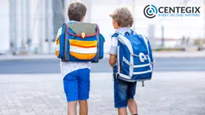 Two young boys wearing backpacks walking outside.