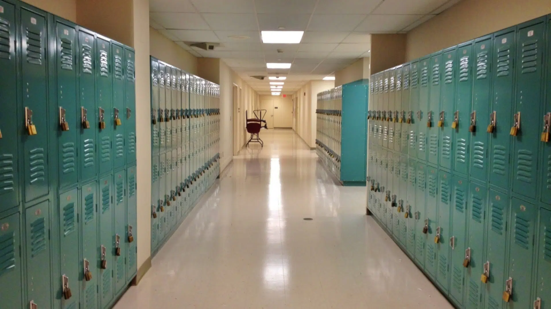 An empty school hallway filled with turquoise lockers.